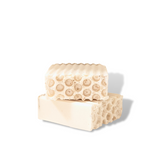 Three natural honeycomb-textured soap bars stacked on a white marble bathroom ledge against a white subway tile wall with water droplets.